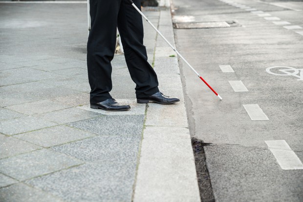 Man stepping off a pavement with a white cane